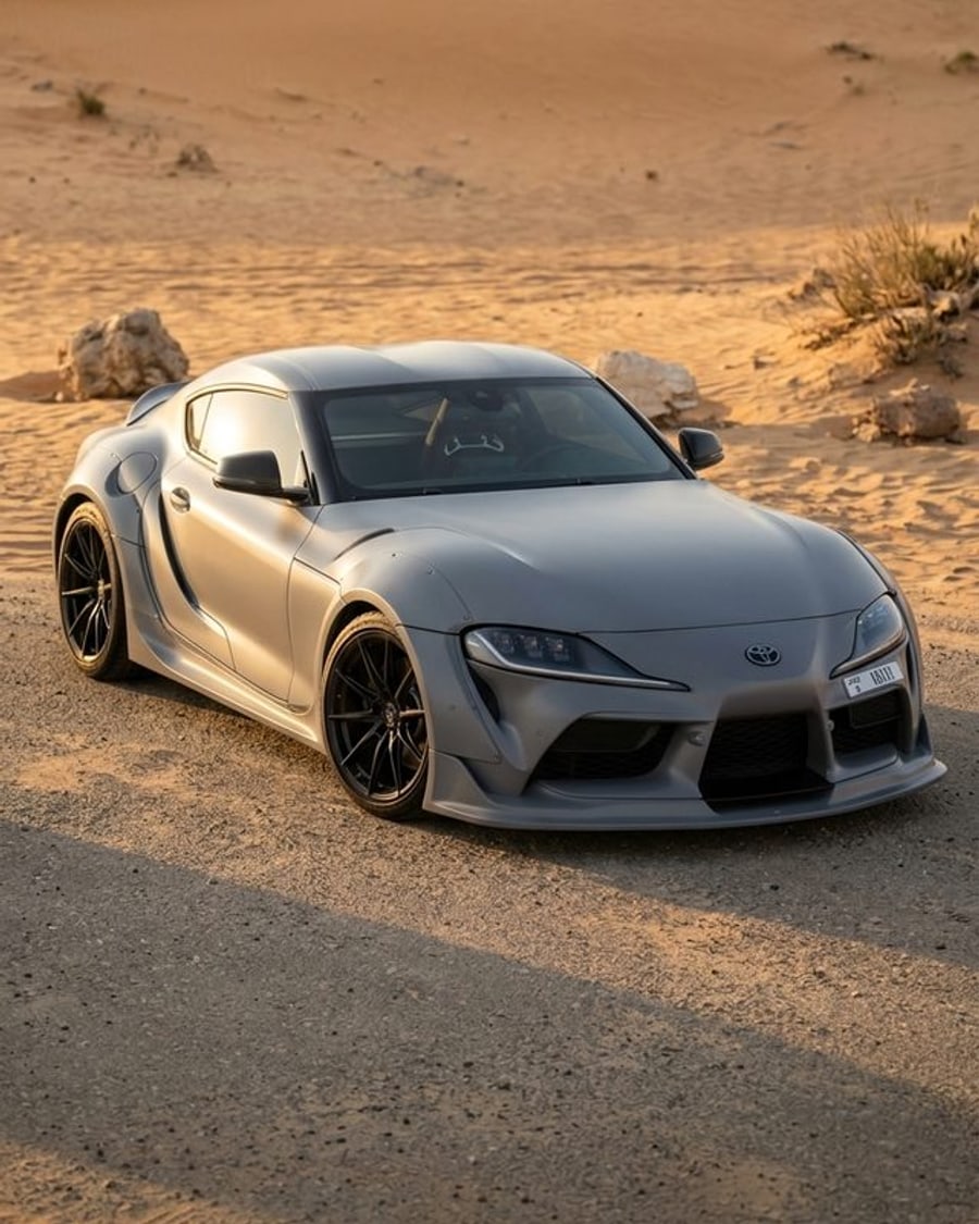 A sports coupé in a satin Nardo grey wrap on a desert road at golden hour, rendered by render360