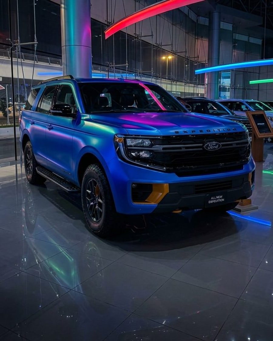 A large SUV in a blue-to-purple colour-shift wrap under neon showroom lighting, rendered by render360